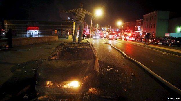 A rioter stands atop a burning car