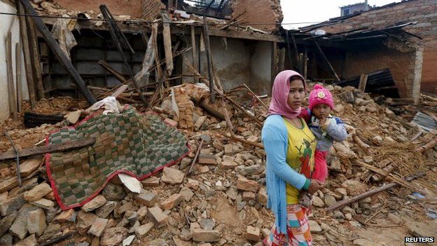 A Nepali woman holds her baby in front of the wreckage of a house that was completely destroyed in Saturday's earthquake in Gorkha, Nepal (30 April 2015)