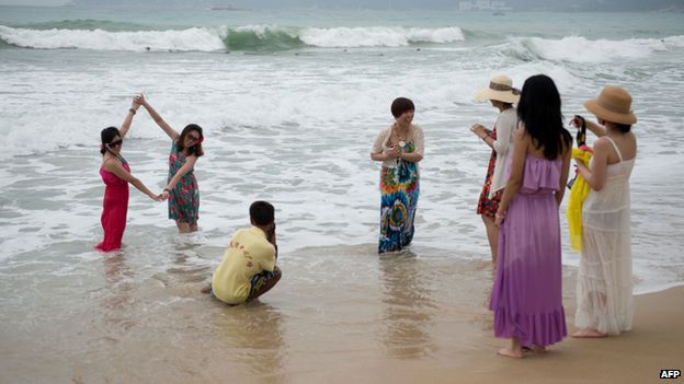 A group of tourists pose for photos in the sea at a beach in the Yalong Bay area of Sanya