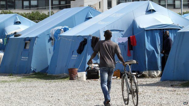 A man pushes a bicycle next to blue tents in the camp