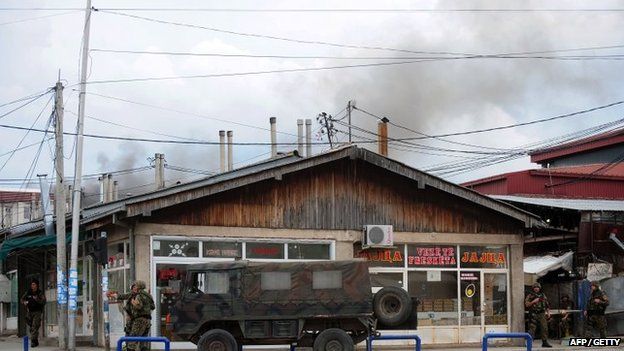 Police officers man a check-point in the conflict zone, as black pillar of smoke is visible behind them, in Kumanovo, northern Macedonia, on May 9, 2015