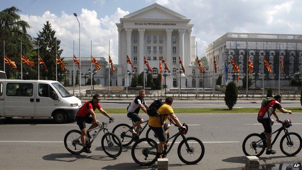People on bicycles pass in front of the Government building where the national flags are lowered at half mast, in Skopje, Macedonia May 10, 2015