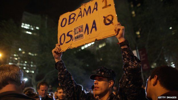 A man holds up a sign reading: "Obama-1, Osama-0"