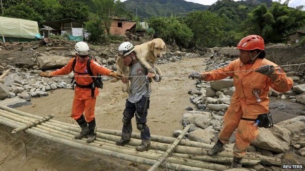 Rescue workers carry a sniffer dog as they cross an improvised bridge to search for victims of a landslide close to the municipality of Salgar on 19 May, 2015.