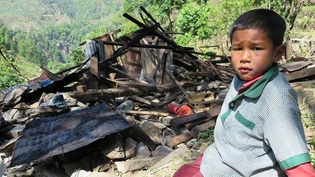 A young boy sits by the rubble of a house in a village in Nepal