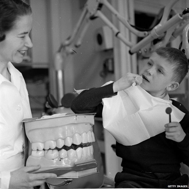 Dental nurse holding big fake teeth to teach young child how to brush