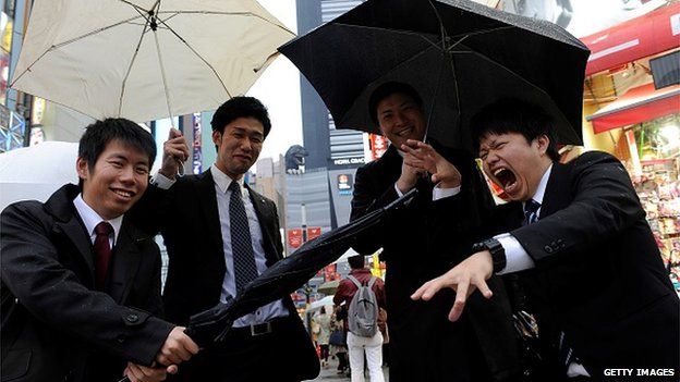 Young salarymen playing on the street while a Godzilla replica is seen behind them in Shinjuku, Tokyo, Japan on 10 April, 2015