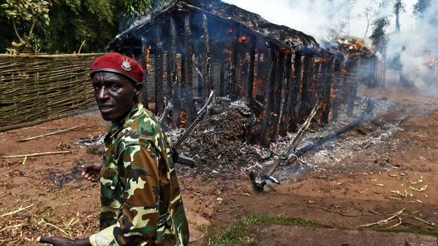 A soldier stands in front of a house set afire by protestors opposed to the Burundian president's bid to stand for a third term in Butagazwa, Mugongomanga, some 30km east of Bujumbura, on 5 June 2015