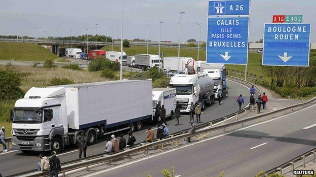 More than a dozen migrants gather near trucks which wait on the road that leads to the Channel tunnel in the hopes of boarding them to make a clandestine crossing to England