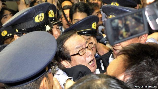 Hiromichi Watanabe (C), chairman of Lower House's Labour committee, surrounded by the Diet guard, tussles with opposition lawmakers as he opens the committee session to pass a controversial bill to revise the worker dispatch law at the National Diet in Tokyo on 12 June, 2015.