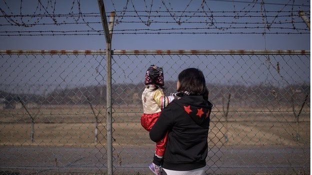 A woman holding a child look towards North Korea as they stand at a military fence at Imjingak park, south of the Military Demarcation Line and Demilitarized Zone (DMZ) separating North and South Korea, on February 19, 2015