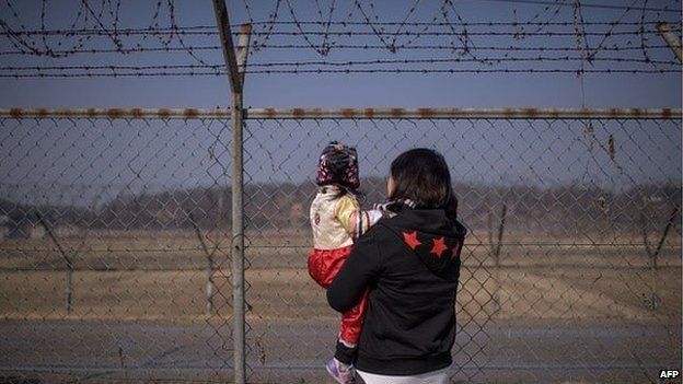 A woman holding a child look towards North Korea as they stand at a military fence at Imjingak park, south of the Military Demarcation Line and Demilitarized Zone (DMZ) separating North and South Korea, on February 19, 2015