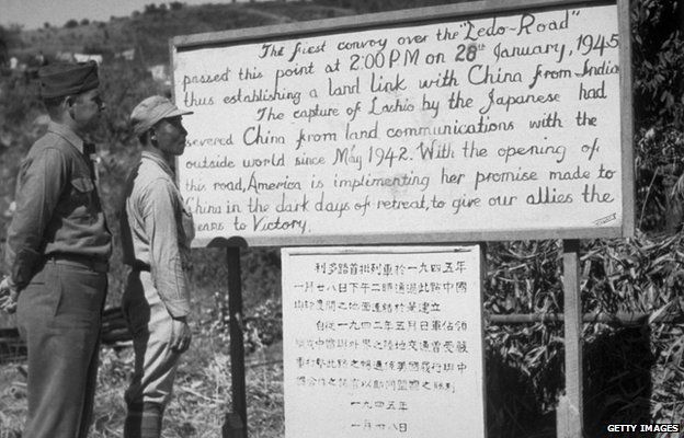 An American and a Chinese soldier reading a sign detailing the first convoy over the Ledo Burma Road, linking China with India.