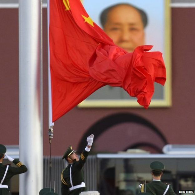 A paramilitary police officer spreads the Chinese national flag out during a flag-raising ceremony in front of a portrait of Mao Zedong at Beijing's Tiananmen Square (11 November, 2013)