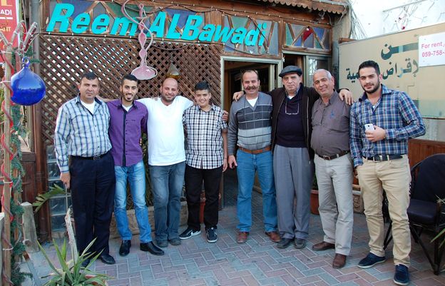 Ocho hombres en la familia Talgieh se paran frente a un café - Los miembros de la familia Thalgieh afuera de la cafetería Reem al-Bawadi - conocidos localmente como la cafetería Abu George. Todos los hombres en la imagen se llaman George o Abu George (el padre de George, ya que su hijo mayor se llama George). George Elias Saba Thalgieh es el segundo desde la derecha, George Nabil George Thalgieh es el segundo desde la izquierda. De hecho, tienes todos los comentarios interesantes que hicieron que grabé incluidos en la función. El mayor George también llamó a su hijo, Khadr, la variante árabe. Se estaba sometiendo a una cirugía cerebral cuando su esposa estaba embarazada y le prometió a San Jorge que llamaría a su hijo por él si le protegía. La señora Thalgieh dijo que era confuso tener un esposo e hijo llamado George, por lo que se establecieron en Khadr. El mayor George,