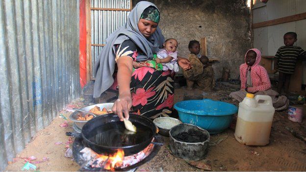 Faduma Aden Mohamud holding a baby as she cooks samosas in her house in a displacement camp in the Somali capital, Mogadishu