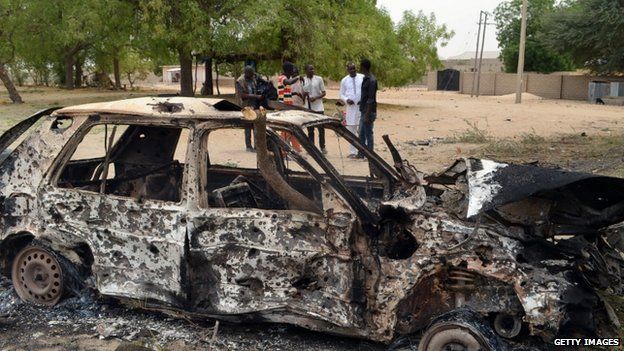 People stand by the wreckage of a car that has been blown up by suspected Boko Haram militants in Nigeria's troubled north-eastern city of Maiduguri on 25 March 2014