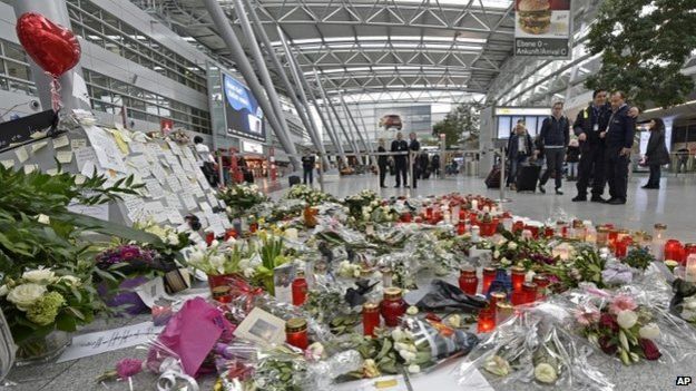 Passengers pass by candles and flowers for the victims of the plane crash at the airport in Dusseldorf (31 March 2015)