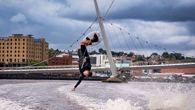 a somersaulting windsurfer is upside down on the river foyle with Derry's peace bridge shown in the background