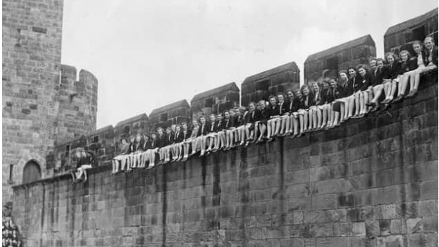 A row of girls sitting on a wall inside Alnwick Castle 