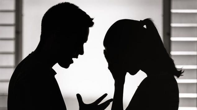 A silhouette of a man and a woman facing each other, standing in front of a window. The woman has her head in her hands and looks upset and distressed, while the man is waving an open palm and seems frustrated and angry