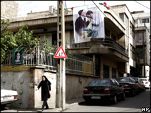 Una mujer pasa bajo un cartel que muestra al presidente de Irán, Mahmoud Ahmadinejad, besando la mano de un anciano, sobre una casa en Teherán