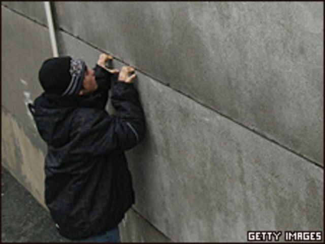 Un joven intenta mirar a través de una grieta en lo que queda del Muro de Berlín