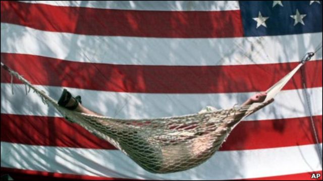 Человек отдыхает в гамаке на фоне американского флага