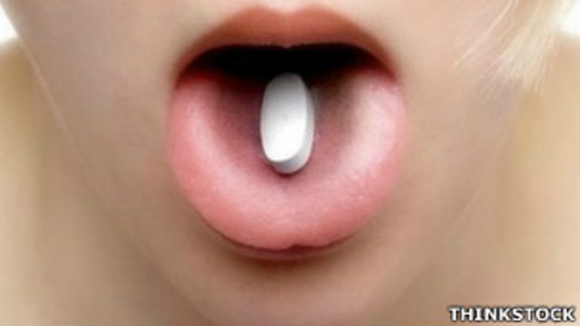 Una píldora de ibuprofeno sobre la lengua de una mujer