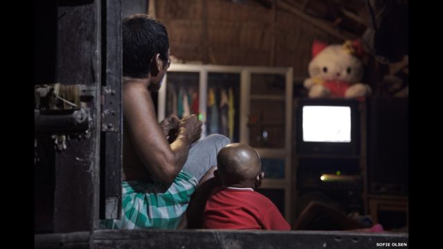 Отец и сын смотрят телевизор в хижине в деревне мокенов на одном из Суринских островов