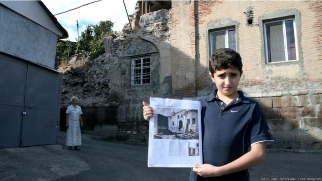 Мальчик показывает старую фотографию мечети, стоя перед разрушающимся зданием. 