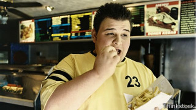 Persona obesa comiendo comida rápida.