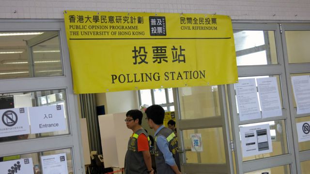 香港新界元朗一處「佔領中環」民間全民投票站門前工作人員列隊歡迎投票市民（BBC中文網圖片29/6/2014）