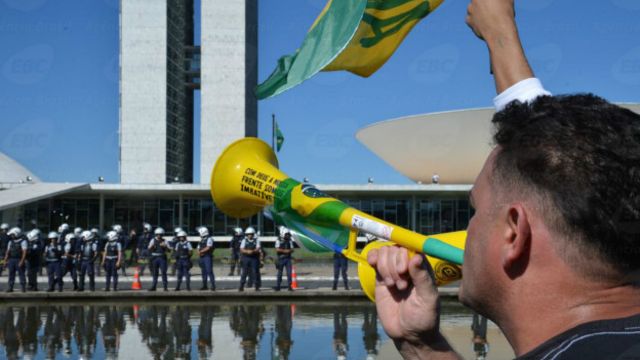 Un manifestante reclama frente al Congreso brasileño, custodiado por policías.