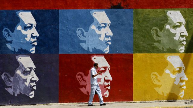 Una persona pasa frente a un mural con rostros de Chávez
