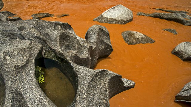 Resíduos em trecho pedregoso do rio Doce em Minas Gerais; no lado esquerdo, pode-se observar a cor original da água, empoçada na rocha