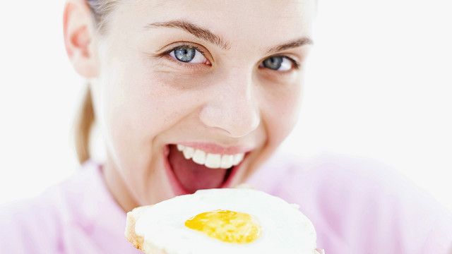 Una mujer comiéndose una tostada de pan con un huevo encima