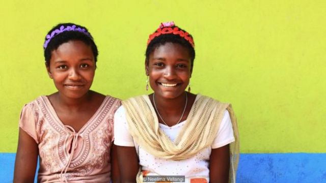 伊丽莎白（Elizabeth）和阿什维尼（Ashwini）两姐妹在加德加拉一座明亮的村屋前微笑

（图片来源：尼莉玛·瓦伦吉 [Neelima Vallangi]）
