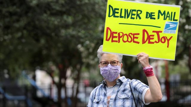Mulher protesta em Washington com placa com os dizeres 'Entregue as correspondências / deponha DeJoy'