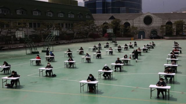 Alumnos surcoreanos dando un examen distanciados en una cancha deportiva.
