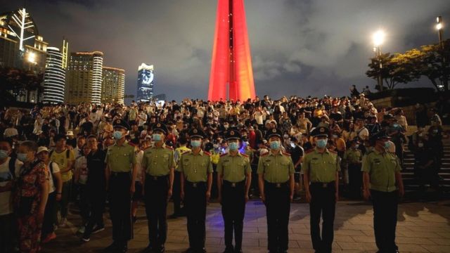 Paramilitary police and police officers keep watch as people gather to they watch a light show celebrating the 100th founding anniversary of the Communist Party of China at The Bund in Shanghai, China, on 30 June 2021