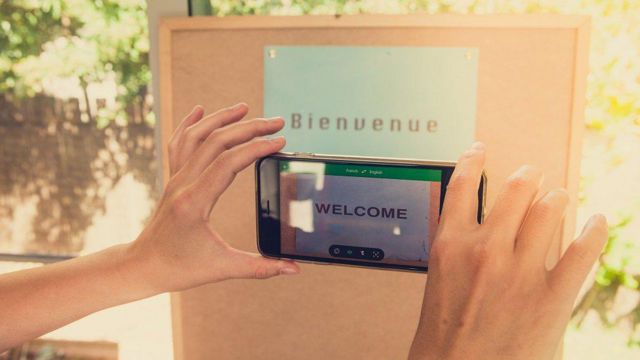 Pessoa apontando o celular para texto em francês, que na tela aparece traduzido para inglês