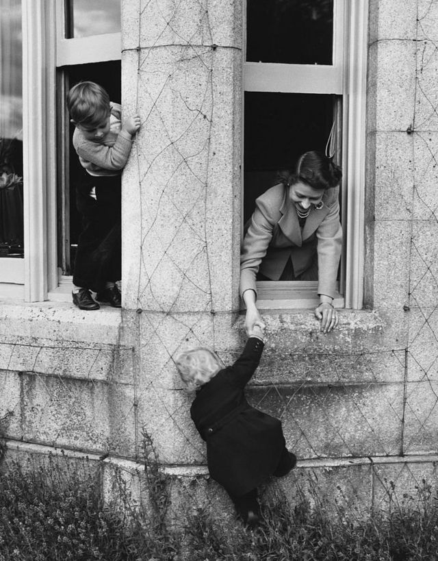 The Queen plays with Prince Charles and Princess Anne in the castle windows in 1952.