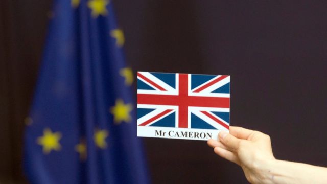 Una tarjeta con la bandera británica y el nombre de David Cameron frente a una bandera de la Unión Europea.