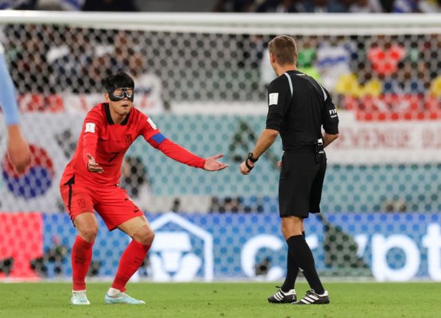 Son Heung-min en la cancha de juego exclamándole al árbitro con sus brazos extendidos.