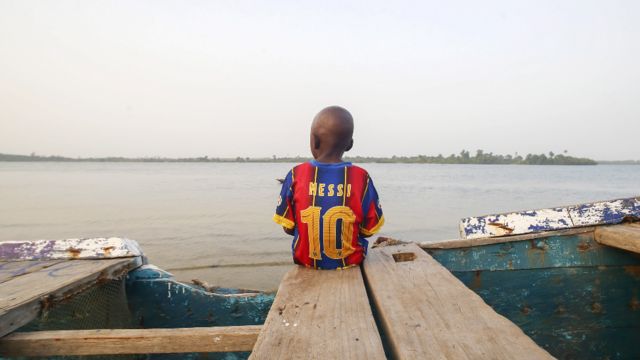 Wani yaro zaune kan kwale-kwalen kamun kifi ya na kallon teku, an dauki hoton bayan rigarsa mai lamba 10 ta dan wasan Barcelona Lionel Messi, a kasar Liberia - ranar Asabar 20 Maris 2021