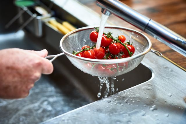 Tomates-cereja sendo lavado na pia da cozinha