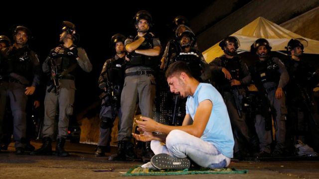 Palestino orando en la calle frente a soldados