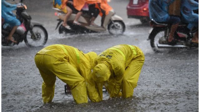 Hai công nhân của công ty thoát nước thành phố Hà Nội mở cống thoát nước trên một tuyến đường bị ngập năm 2017