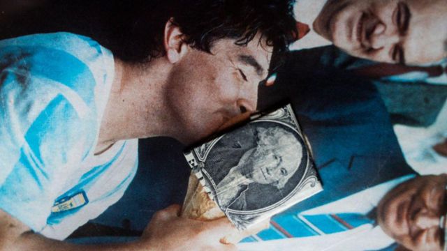 Billete de dólar sobre la imagen de Diego Maradona besando la Copa del Mundo de fútbol de 1986